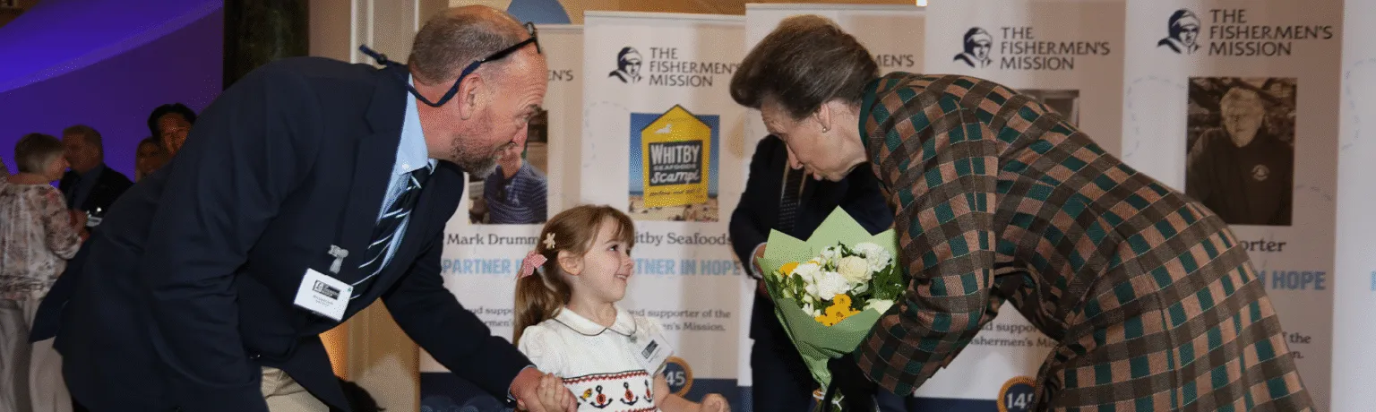 HRH Princess Royal talks to a child who is accompanied by her father, while accepting a bouquet.